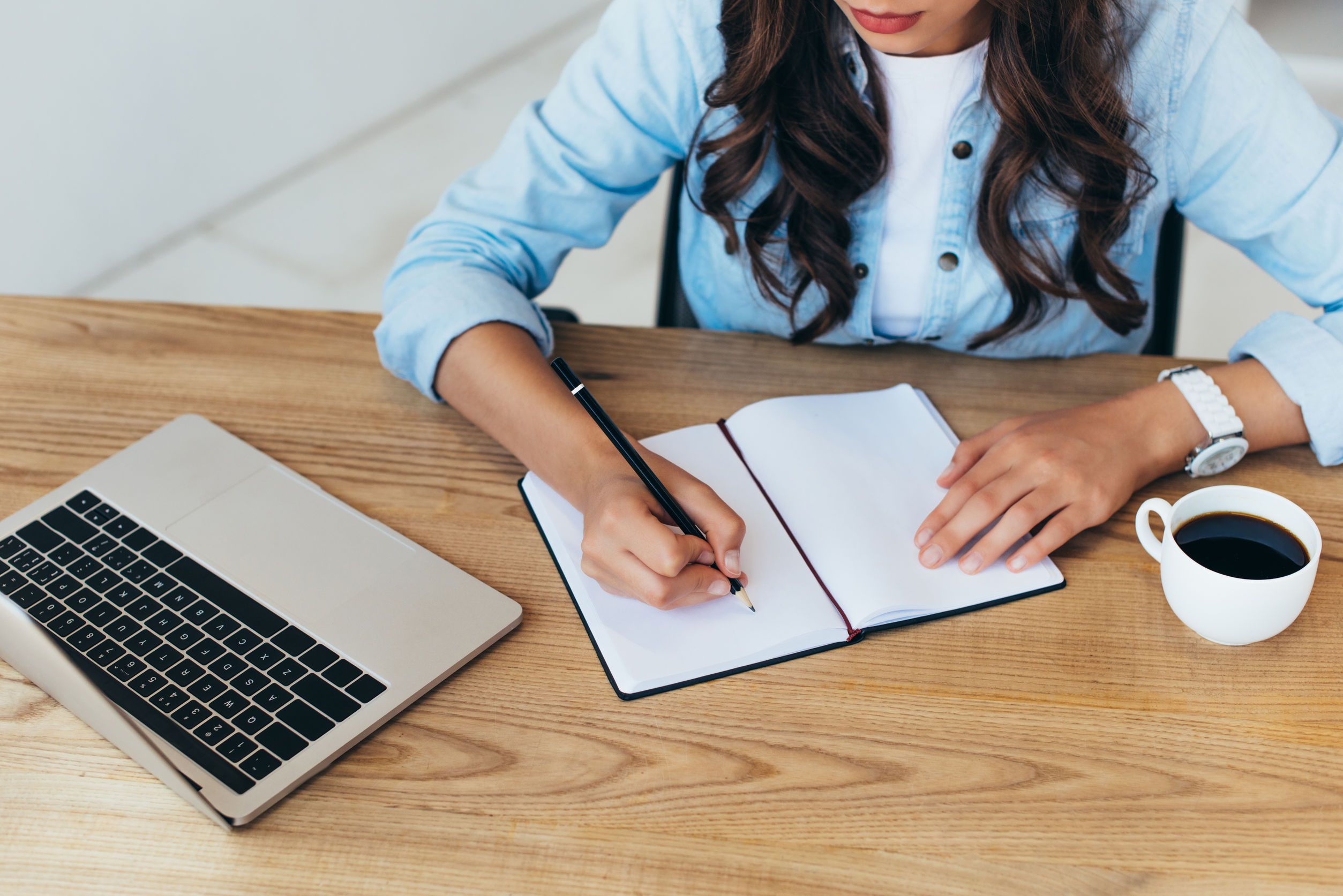 partial view of woman taking notes while taking part in webinar in office