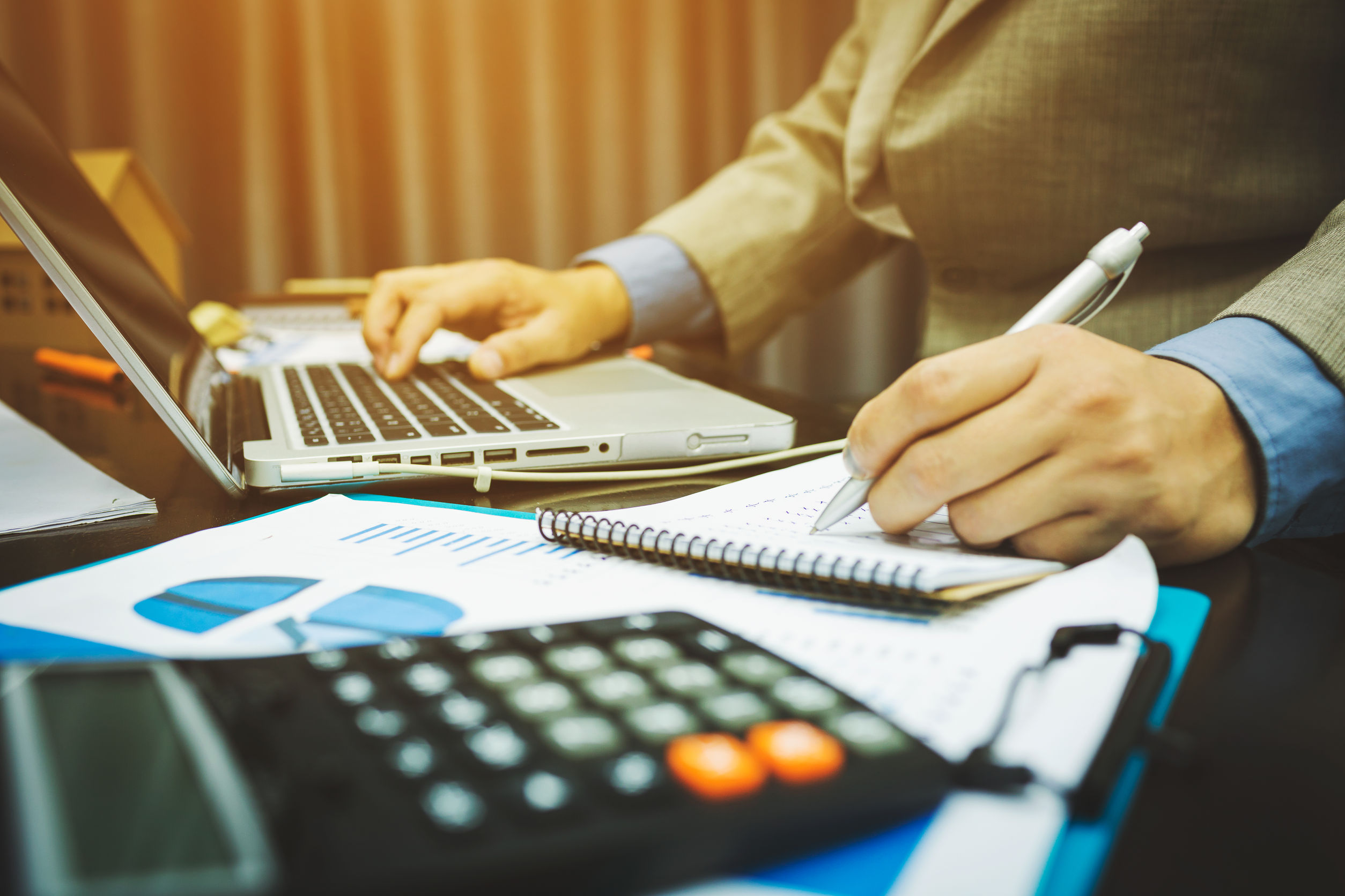 Person sitting at desk with laptop and calculator doing his taxes.