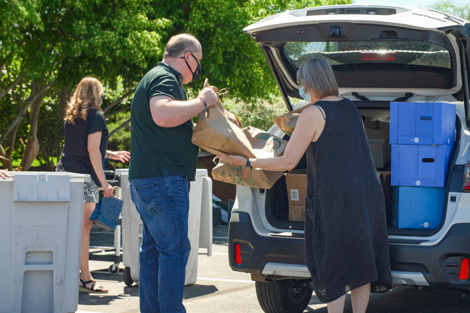 Shred Day attendees removing bags of shred material from the trunk of an SUV.