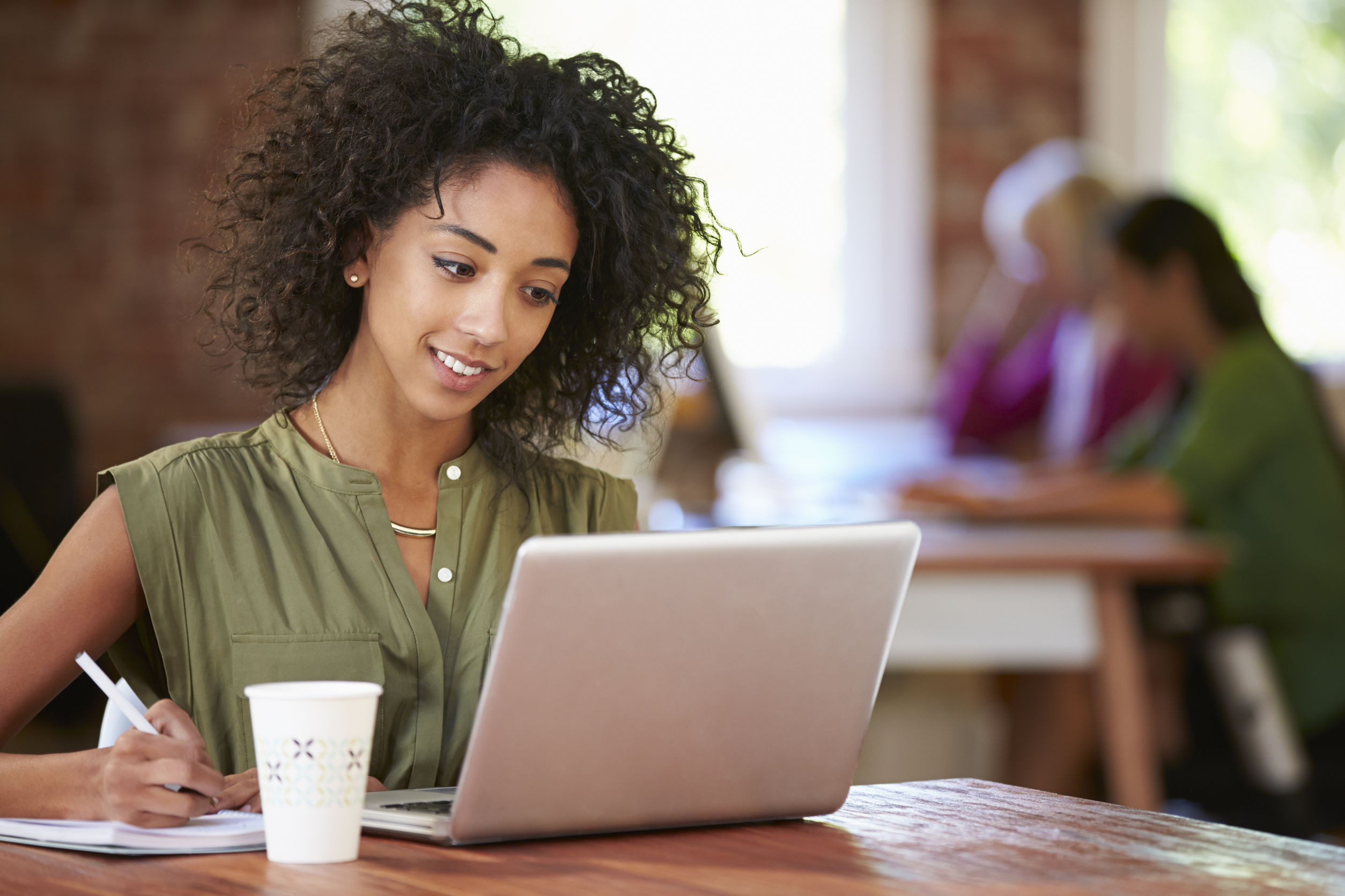 Photo description: Woman taking notes while watching online class on her laptop.