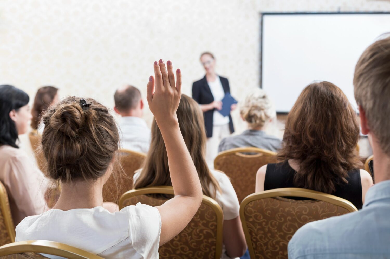 Photo description: listener raising hand to ask question during seminar.