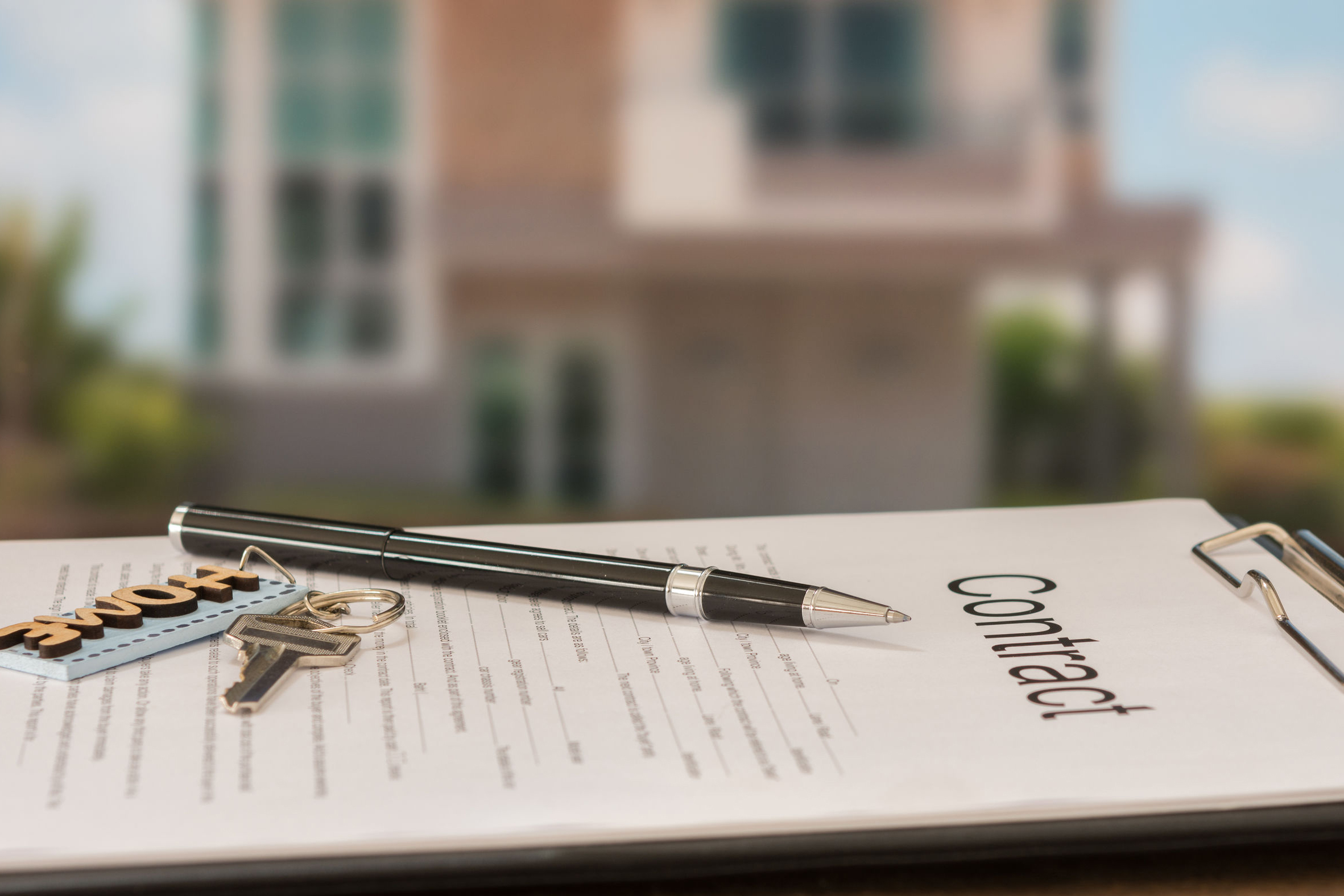 Image description: Closeup pen on contract document with house in background.