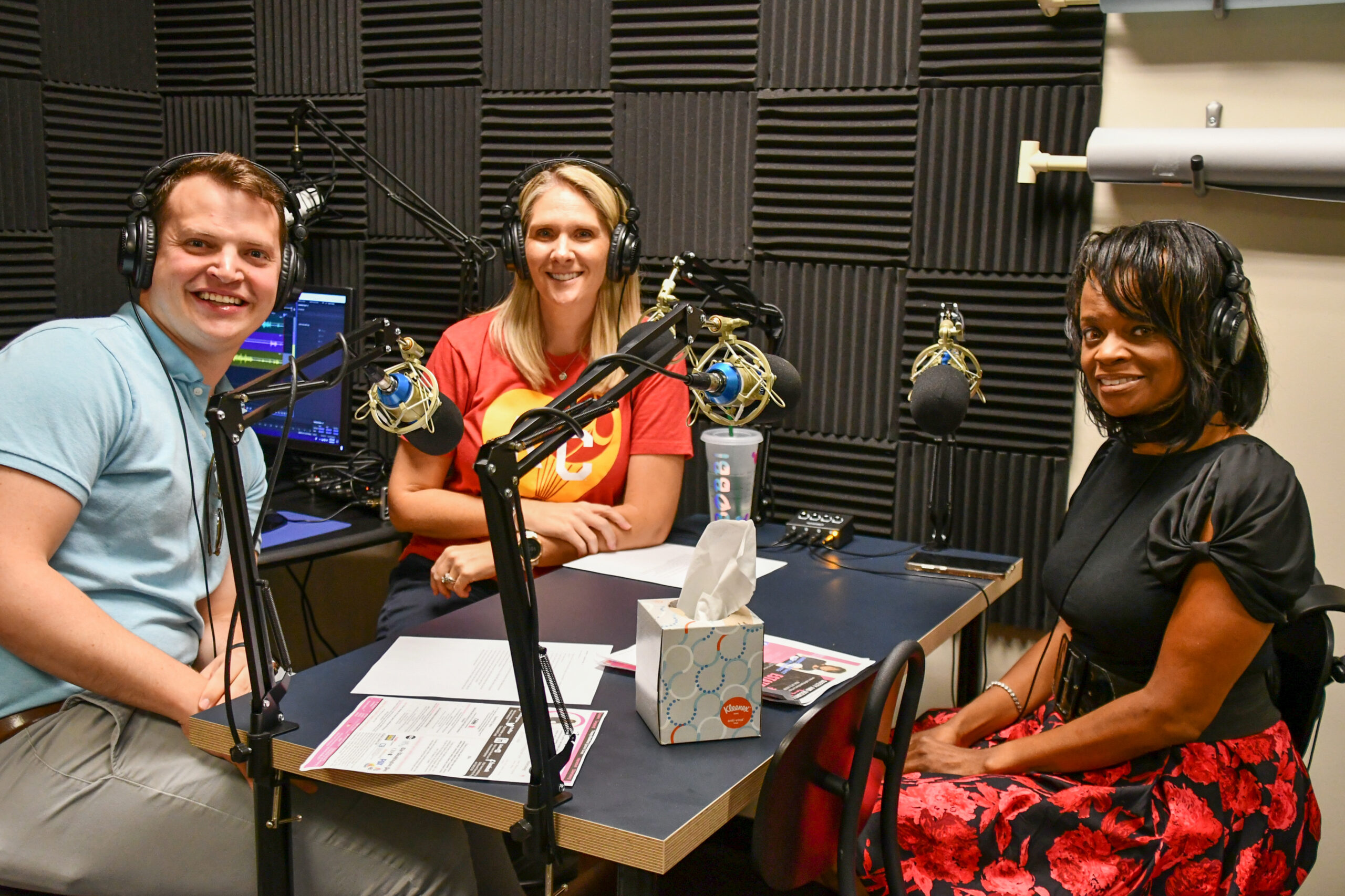 Image description: Kansas City RealTalk hosts Bobbi and Alex sit across the mics from safety expert Tracey Hawkins as they record a 2019 episode.